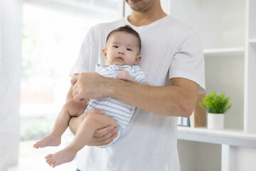A man is holding a baby in his arms. The baby is wearing a blue and white striped shirt. The man is smiling at the baby, and the baby is looking up at him
