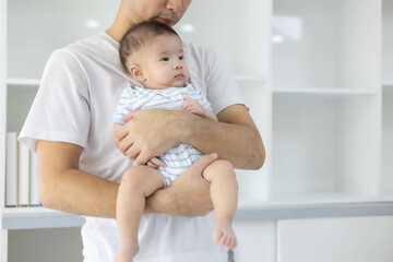 A man is holding a baby in his arms. The baby is wearing a blue and white striped shirt. The man is smiling at the baby, and the baby is looking up at him
