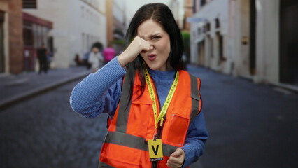 Fototapeta premium Brunette woman in orange vest volunteering on old town street with happy expression emphasizing community spirit and engagement in vibrant city setting