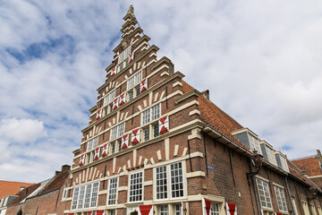 Dutch architectural gem with a distinct stepped gable, showcasing traditional brickwork and red and white shutters against a bright sky. A historical building in Leiden reflecting European heritage.