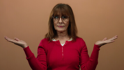 Senior hispanic woman in a red sweater poses thoughtfully with arms extended against a brown...