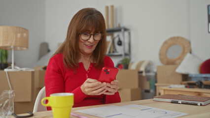 Senior woman in new home living room joyfully using smartphone surrounded by moving boxes showcasing a fresh start and connection