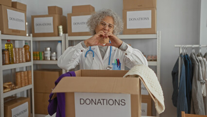 Woman sorting donations in indoor charity center surrounded by labeled boxes and clothing items,...