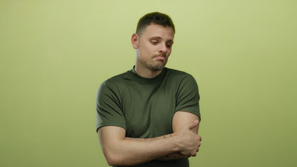 Young man with beard and tattoos stands isolated against a yellow background expressing indecision...