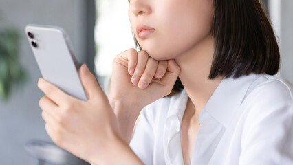 スマートフォンを持って考えごとをする女性