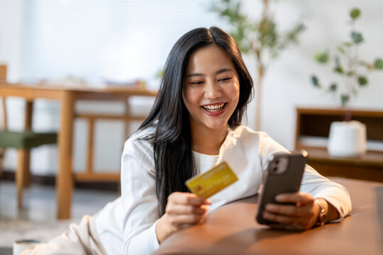 A woman is smiling while holding a credit card and looking at her phone