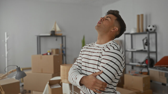 Young man standing with arms crossed in a new home living room surrounded by boxes and decor, creating a vibrant atmosphere.