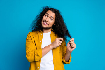 Young man in casual yellow shirt styling hair with a comb while smiling playfully against a bright...