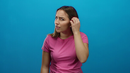 Woman in pink shirt listens with hand to ear against blue background showing curiosity and interest...