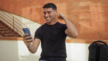 Young man celebrating with smartphone outdoors displaying joy and success in urban setting