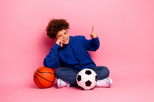 Fototapeta Charming young boy gesturing happily while sitting with sports equipment against a bright pink background
