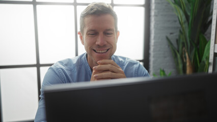 Handsome man smiling in modern office room with natural light gently illuminating his face, showing...