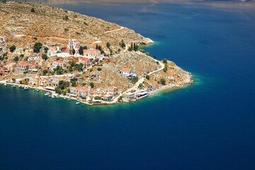 View of Ano Symi shore from a higher point, sun shines on traditional Mediterranean architecture building near sea