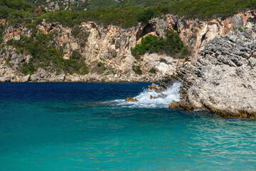 Sea crashing on rocks near calm water at Glyko beach in Liapades, sun shines to rocky shore background