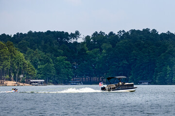 Obraz premium Pontoon boat pulling inflatable tube float raft on lake. Family on a pontoon party boat enjoying tubing on a summer day with their children.