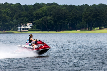 Teenage boy riding jet ski personal watercraft and enjoying summer day on lake.