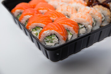 Delicious dinner, on the table various Sushi rolls with salmon, tuna, smoked eel, avocado, cream cheese laid out in a box. Sushi menu. Top view of various sushi. Holding sushi with chopsticks.