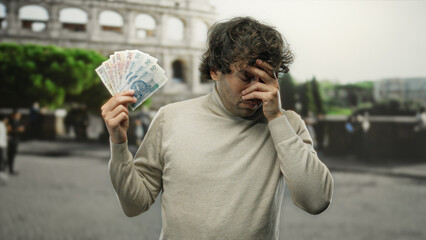 Hispanic man outdoors near the roman colosseum in rome looking worried while holding polish zloty banknotes, surrounded by city life and tourist attractions.