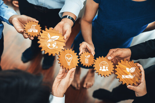 A diverse team collaborates with wooden gears featuring eco-friendly and innovative icons, symbolizing their commitment to sustainable business practices and growth. Amity