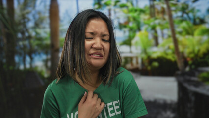 Woman in green volunteer shirt showing disgust in outdoor park setting amidst lush greenery,...