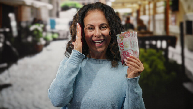 Woman smiling while holding new zealand banknotes outdoors on a restaurant terrace, showcasing happiness and middle age life.