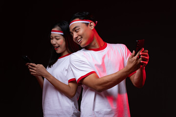 Portrait of Young Asian Man and Woman with Phone Wearing Red White Outfit, Indonesia Independence Day Concept