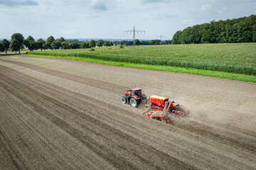 Traktor mit moderner Direkt - Sämaschine beim Drillen auf einem staubigen Feld, Luftbild.