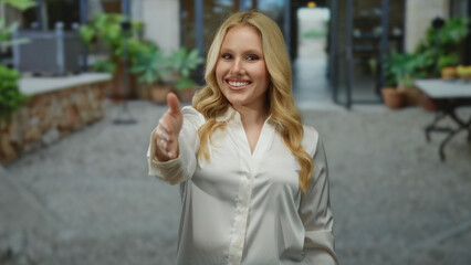 Woman smiling with extended handshake in city street background, blonde young female in white shirt...