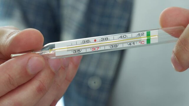 Measuring temperature with a mercury thermometer during a cold.
A sick man measures his body temperature with a mercury thermometer.
Fever and weakness in the body.
Pain, virus, mercury