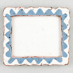 Handmade ceramic tile frame with decorative painted border in blue and white watercolor style. Artisan pottery square with ornate edge design creates rustic Mediterranean inspired accent piece