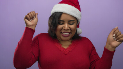 Woman in red sweater and santa hat dancing joyfully against a purple background celebrating christmas cheer with a happy expression