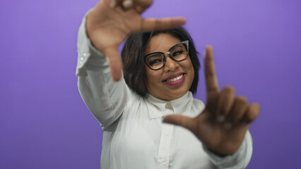 Woman smiling and framing with hands, wearing glasses on a purple background, conveying positivity...