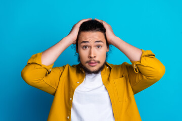 Surprised young man gesturing with hands on head against a bright blue background showcasing...