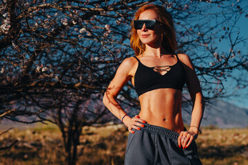 Young beautiful fitness woman posing in garden on mountains background
