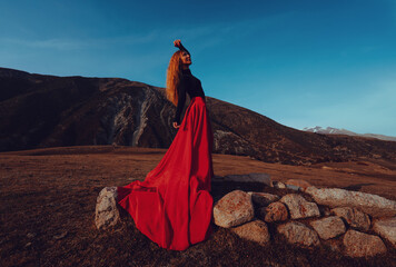 Young beautiful woman dancer in red dress standing in high mountains in the evening