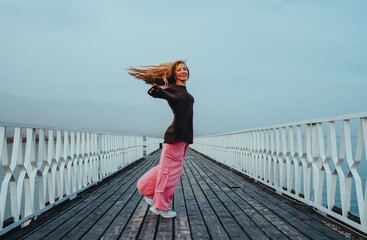 Young woman dancing on pier on lake shore on summer day