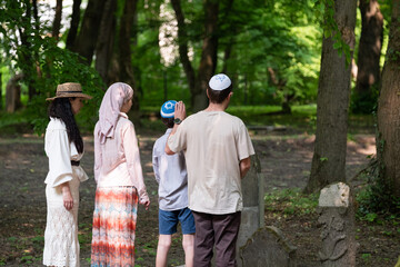 Mother, father, daughter and son jews at jewish cemetery pay respect to ancestors, jewish woman in wig and hat and long skirt, boy in kippah, girl in headscarf, jewish family
