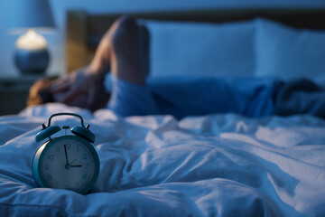 Frustrated man suffering from insomnia on bed indoors, focus on alarm clock