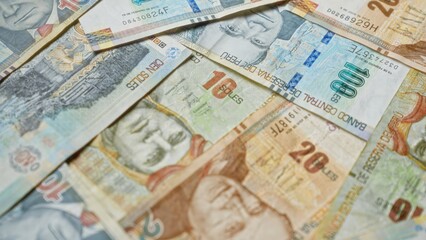 Peruvian currency notes of various denominations spread out in a close-up view, depicting different historical figures and vibrant designs.