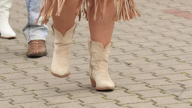 Group of men and women performing a lively line dance in cowboy outfits to country music. Energetic choreography, synchronized steps, Western style, outdoor fun and unity.