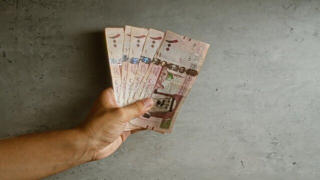 Man holding saudi riyal banknotes against a concrete background, showcasing currency.