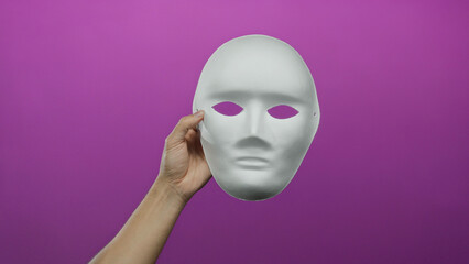 Man holding a blank white mask against a vibrant pink background, showcasing elements of anonymity and creativity isolated in a studio shot.