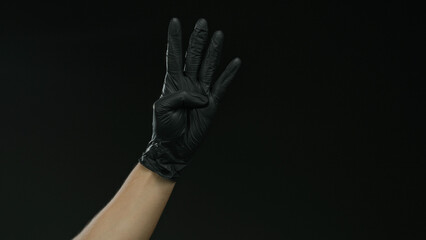 Man with glove displaying three fingers against a dark background, highlighting protection and mystery in an isolated setting.