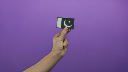 Man holding embroidered pakistani flag against purple background with isolated wall setting.