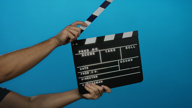 Male hand holding clapperboard against blue background ready for action in film production scene.