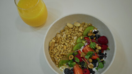 Healthy breakfast bowl with granola, fresh fruit, and nuts next to a glass of orange juice on a restaurant table.