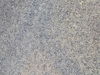 Detailed view of a rough gray asphalt surface featuring small gravel stones, ideal for background or texture purposes.