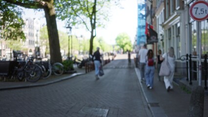 Defocused scene in amsterdam with blurred people walking along a tree-lined street, showcasing urban life and bicycles in a vibrant city atmosphere.
