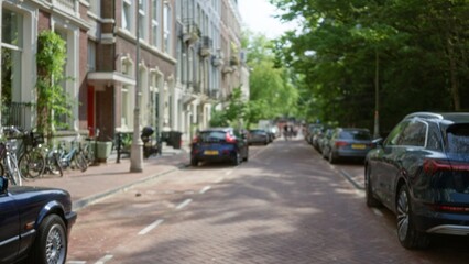 Defocused view of a classic amsterdam street with parked cars, bicycles, and lush greenery, capturing the essence of an urban netherlands setting on a sunny day.
