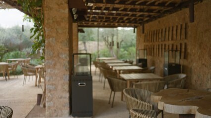 Blurred view of a mediterranean terrace restaurant with empty wooden tables and chairs under a stone pergola, highlighting a peaceful and serene outdoor setting.